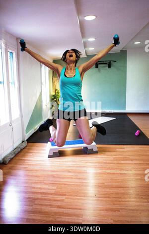 Femme sautant avec une étape et des haltères célébrant la réalisation de fitness Banque D'Images