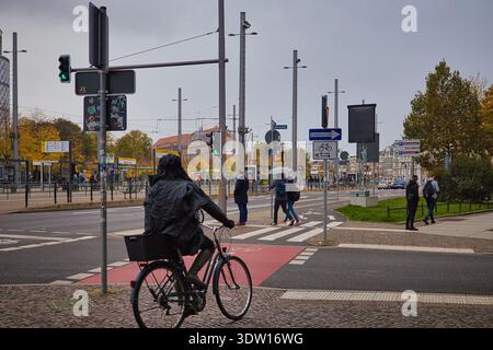 Cycliste en poncho de pluie à Goerdelerring à Leipzig ; circulation automnale de la ville avec piétons, feux de circulation et marquage rouge des pistes cyclables Banque D'Images