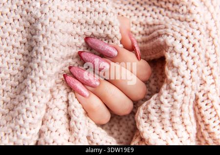 Main de femme arborant une manucure rose élégante avec un design complexe, reposant sur un pull confortable texturé Banque D'Images