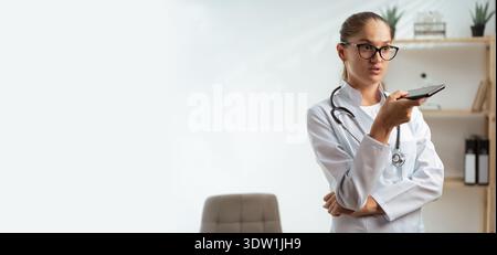 Jeune femme médecin en manteau blanc et lunettes de commande à ai assistant utiliser la voix par téléphone. Concept d'intelligence artificielle dans medicare. Banque D'Images