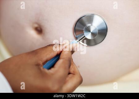 Médecin féminin noir examinant une femme caucasienne enceinte avec stéthoscope Banque D'Images