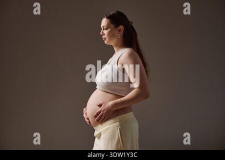 Femme jeune adulte caucasienne tenant le ventre enceinte debout dans le profil Banque D'Images