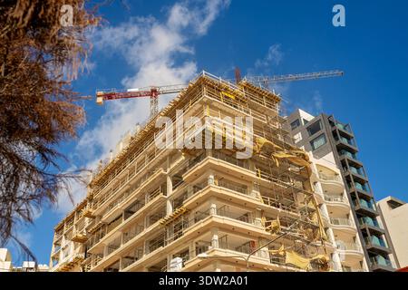 Un bâtiment résidentiel moderne de plusieurs étages en construction avec une grue à tour contre un ciel bleu vif à Malte. Concept de développement urbain. Banque D'Images