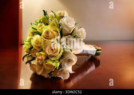 bouquet de mariée formel avec des roses fraîches blanches et crème décorées de cristaux chatoyants, reposant sur une surface en bois poli avec une douce chaleur Banque D'Images