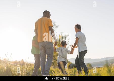 Père afro-américain se promène avec ses enfants dans la nature pendant le coucher du soleil, partageant des moments heureux et se liant en famille. Banque D'Images