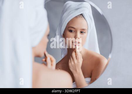 Femme appliquant Lip Gloss devant le miroir après la douche dans la salle de bain Banque D'Images