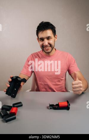 Portrait vertical d'un vidéaste sympathique présentant le grip de la batterie de l'appareil photo et les batteries supplémentaires, donnant un geste du pouce indiquant l'approbation pour la fiabilité Banque D'Images