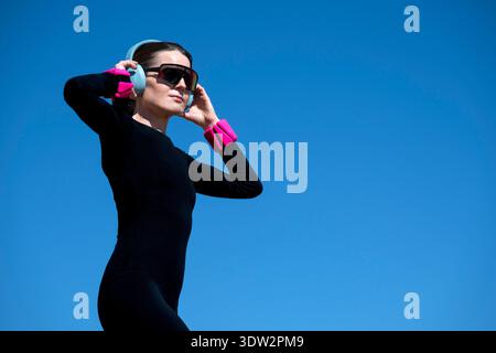 femme pilates portant des poids de poignet réglables et des écouteurs, fond de ciel bleu Banque D'Images