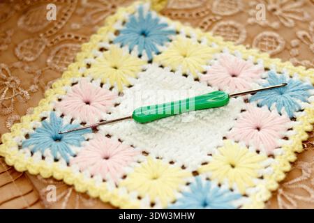 Gros plan d'un projet de crochet de style vintage. Un crochet vert se trouve sur un carré de grand-mère fait à la main avec des fleurs pastel. Un éclairage doux met en valeur le confortable, han Banque D'Images