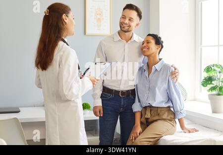 Souriant jeune couple heureux assis avec une thérapeute de médecin de famille féminine dans la clinique médicale. Banque D'Images