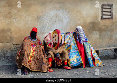 Trois individus sont assis ornés de vêtements traditionnels vibrants. Banque D'Images