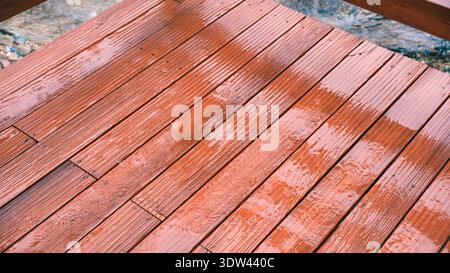Texture détaillée de planches en bois brun recouvertes de gouttelettes d'eau de pluie avec une réflexion douce sous lumière naturelle pour l'arrière-plan Banque D'Images
