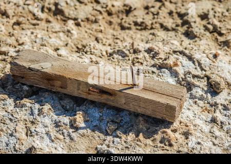 Planche de bois altérée avec des clous rouillés reposant sur un sol rocheux sablonneux sous la lumière du soleil rude dans un paysage côtier aride Banque D'Images
