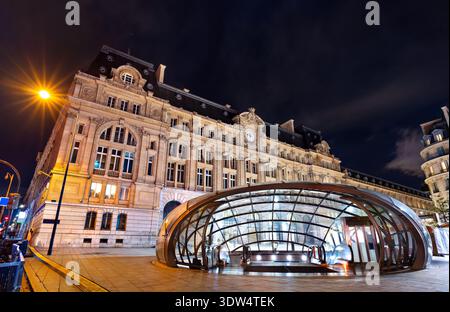 Vue nocturne d'une entrée de métro moderne en dôme de verre devant le bâtiment historique illuminé de la gare Saint Lazare à Paris, France. Banque D'Images