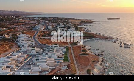 Villas de luxe modernes et propriétés résidentielles bordent la côte pittoresque de Chypre, avec piscines privées et vue sur la mer Méditerranée pendant le magnifique coucher de soleil de l'heure dorée. Vue aérienne Banque D'Images
