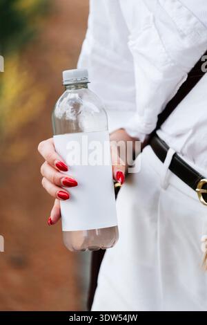 Gros plan d'une femme tenant une bouteille d'eau en plastique sans marque avec étiquette vierge à l'extérieur, espace de copie pour le marquage. Banque D'Images
