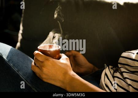 gros plan de la main de la femme tenant une tasse de café chaud avec fumée vapeur le matin, vraie routine à la maison confortable Banque D'Images
