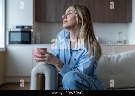 Détendu rêvé femme d'âge moyen profite lentement consciente pause café reconnaissant sur canapé confortable à la maison Banque D'Images