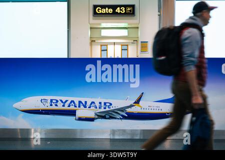 Passager avec sac à dos marchant rapidement devant une grande publicité Ryanair mettant en vedette un avion à l'aéroport de Stansted Banque D'Images