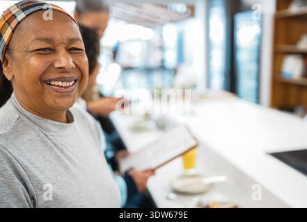 Femme afro-américaine mangeant le petit déjeuner à l'intérieur d'un café-bar tout en souriant à la caméra pendant l'heure du matin - nourriture saine et concept de style de vie des gens Banque D'Images