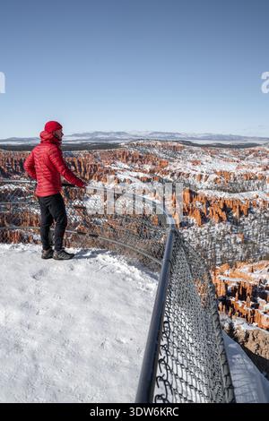 Vue d'une veste rouge éclatante contre le précipice enneigé et les hoodoos chauds et terreux debout dans le paysage givré, Bryce Canyon City, Utah, Uni Banque D'Images