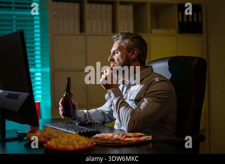 Freelance manger de la pizza tard le soir. Bureau de nuit avec ordinateur portable et collation. Détente au bureau de nuit. Travail de nuit. Homme d'affaires mangent collation tout en travaillant sur Banque D'Images