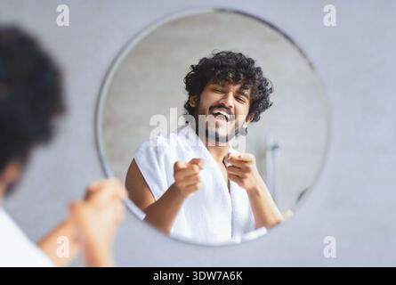 Homme se tient devant miroir et sourires tout en pointant son reflet dans la salle de bain Banque D'Images