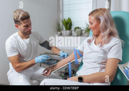 Un travailleur de la santé masculin prélève du sang dans un bras de patiente dans une clinique médicale moderne. Banque D'Images