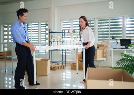 Les adultes asiatiques qui déplacent avec joie un colis dans un cadre de bureau contemporain signifient un nouveau départ et des services de livraison efficaces Banque D'Images