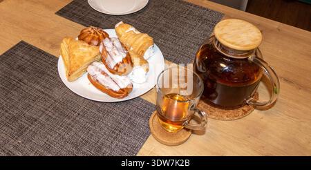 Divers bonbons cuits au four sur l'assiette et du thé dans une tasse et une théière Banque D'Images