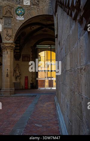 Une vue à travers une ancienne arche en pierre dans une cour lumineuse, mettant en valeur les bâtiments italiens traditionnels. Banque D'Images