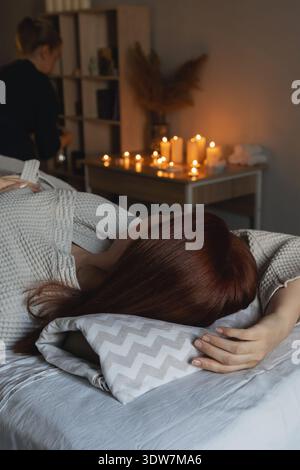 Femme allongée sur une table de massage, recevant un soin spa relaxant entouré de bougies allumées, créant une atmosphère de bien-être apaisante Banque D'Images