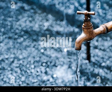 L'eau coule d'un robinet en laiton vintage sur un fond bokeh bleu, symbolisant la rareté de l'eau et la gestion des ressources Banque D'Images