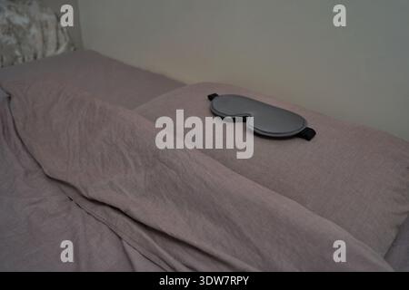 Masque de sommeil gris reposant sur un lit soigneusement fait avec des draps gris doux dans un cadre de chambre calme. Banque D'Images