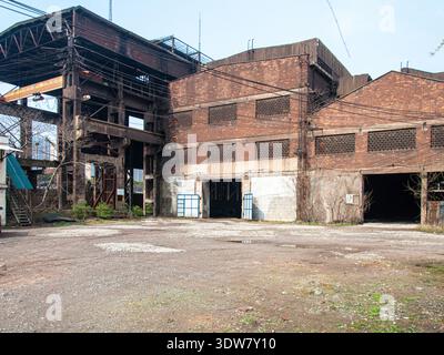 Vue extérieure large d'un grand bâtiment d'usine de briques rouges abandonné avec des fenêtres manquantes et une structure en acier exposée attachée. Banque D'Images