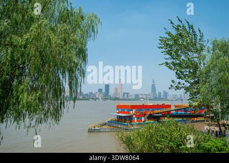 Vue de paysage horizontal d'une rivière boueuse et des quais flottants colorés, encadrés par des branches d'arbre de saule vert au premier plan, avec une ligne d'horizon de la ville être Banque D'Images