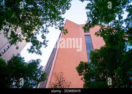 Vue imprenable sur la façade d'un bâtiment aux carreaux rougeâtres encadrée par la verdure des arbres. Banque D'Images