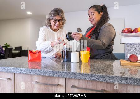 Deux femmes faisant du café avec une presse française, partageant un moment heureux dans la cuisine Banque D'Images