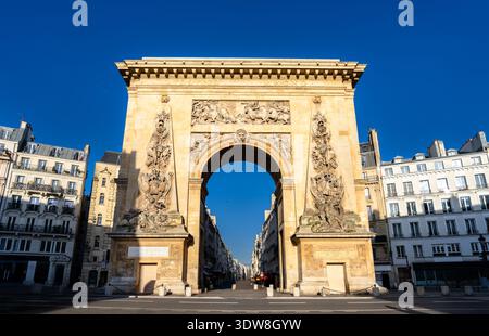 Vue panoramique ensoleillée sur l'arc de triomphe historique de la porte Saint-Denis avec des sculptures en bas-relief complexes et des bâtiments parisiens classiques à Paris, France. Banque D'Images