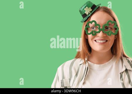 Rousse jeune femme dans le chapeau de leprechaun avec des lunettes sur fond vert, gros plan. Célébration de la fête de Patrick Banque D'Images