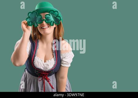 Serveuse irlandaise rousse dans le chapeau leprechaun avec des lunettes en forme de trèfle sur fond vert. Célébration de la fête de Patrick Banque D'Images