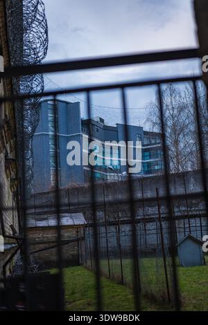 Barreaux de prison sombres et cadre de fil de rasoir Lukiskes prison à Vilnius, Lituanie, comme une grande tour bleu gris avec des fenêtres en ruban s'élève au-delà d'un mur de pierre dedans Banque D'Images