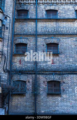La prison de Lukiskes à Vilnius, en Lituanie, montre quatre fenêtres cintrées avec des grilles, du fil de rasoir à chaque niveau, les numéros rouges 1 et 2, et un tuyau d'évacuation central i. Banque D'Images