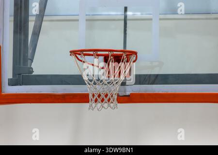 Un panier de basket-ball et un filet se trouvent dans une salle de sport scolaire avec un mur blanc en arrière-plan. Banque D'Images