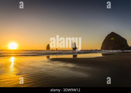 Le soleil se couche sur l'océan, projetant une lueur chaude sur la plage. Les vagues vacillent doucement sur le rivage, et le ciel est un beau mélange d'oran Banque D'Images