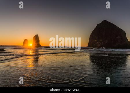 Le soleil se couche sur l'océan, projetant une lueur chaude sur l'eau. Le ciel est un mélange de teintes orange et rose, créant une atmosphère sereine et paisible Banque D'Images