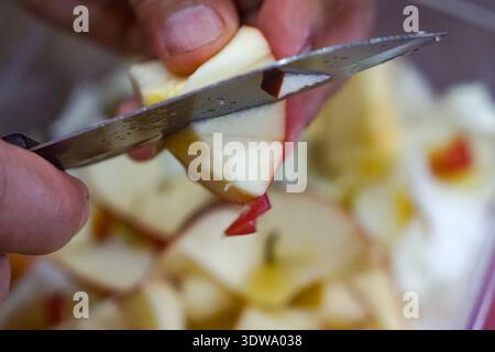 Gros plan de la main tranchant la pomme rouge avec couteau sur la table de cuisine. Banque D'Images