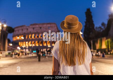 Jeune femme en chapeau admirant le Colisée illuminé dans la soirée à Rome, Italie Banque D'Images