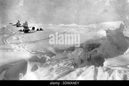 Cette photographie historique de 1913 capture les membres de l'expédition au pôle Sud de Roald Amundsen se reposant, enveloppés de couvertures, au milieu d'un vaste paysage glacé. L'image en noir et blanc traduit la beauté et les conditions difficiles de l'exploration polaire au début du XXe siècle. Banque D'Images