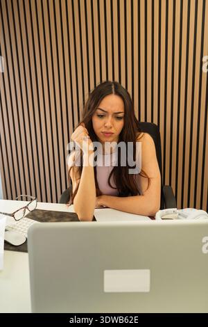 Femme se sentant perplexe tout en se concentrant sur son ordinateur portable à un bureau Banque D'Images